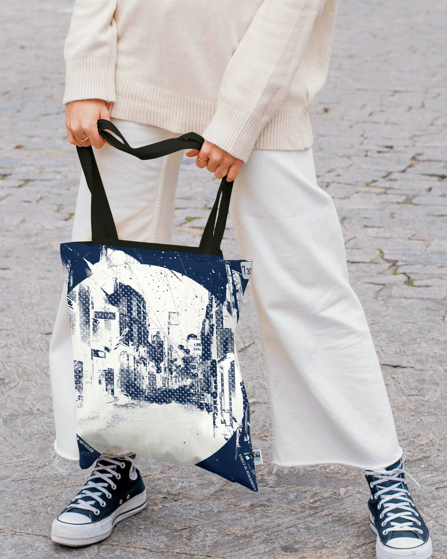 Person holding a tote bag with a cityscape design on a stone pavement.
