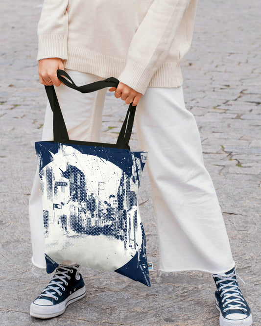 Person holding a tote bag with a cityscape design on a stone pavement.