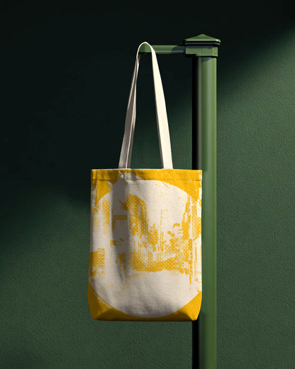 Tote bag with yellow and white design hanging on a green pole against a dark background